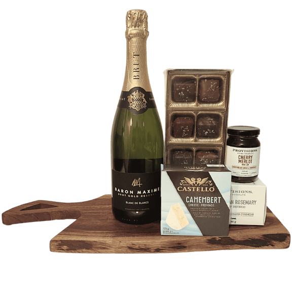 Bottle of Baron Maximilien champagne on a wooden board with Castello Camembert cheese, chocolate truffles, and cherry merlot jam.