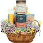 A honey wicker basket featuring pastel-toned spa items, tea, candle, and chocolate bark.