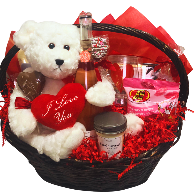 A unwrapped romantic gift basket showcasing a plush teddy bear, wine glass, chocolates, caramel popcorn, candle, and bath soak. 