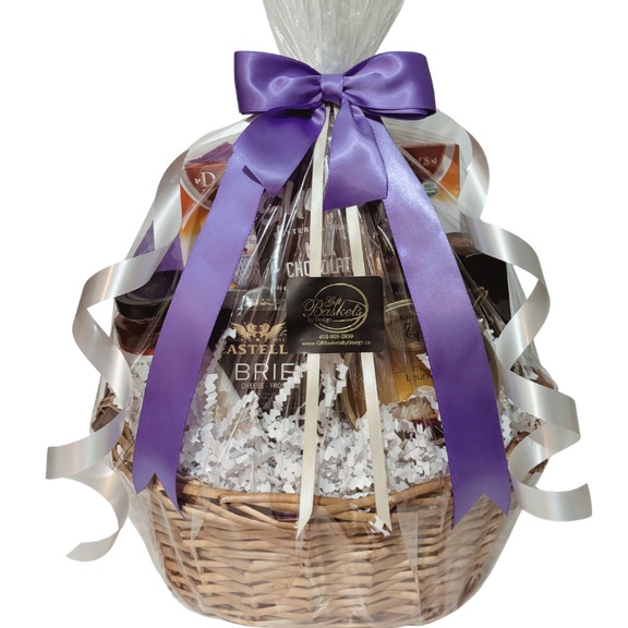 Afternoon tea gift basket with organic teas, artisan cheese, crackers, preserves, and sweets in golden wicker basket with purple and white ribbons and bow.