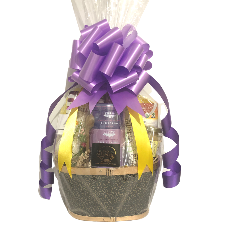 A calming gift basket featuring assorted teas, honey, a bath bomb, chocolate, and snacks, wrapped in cellophane with purple and yellow ribbons, and purple bow.